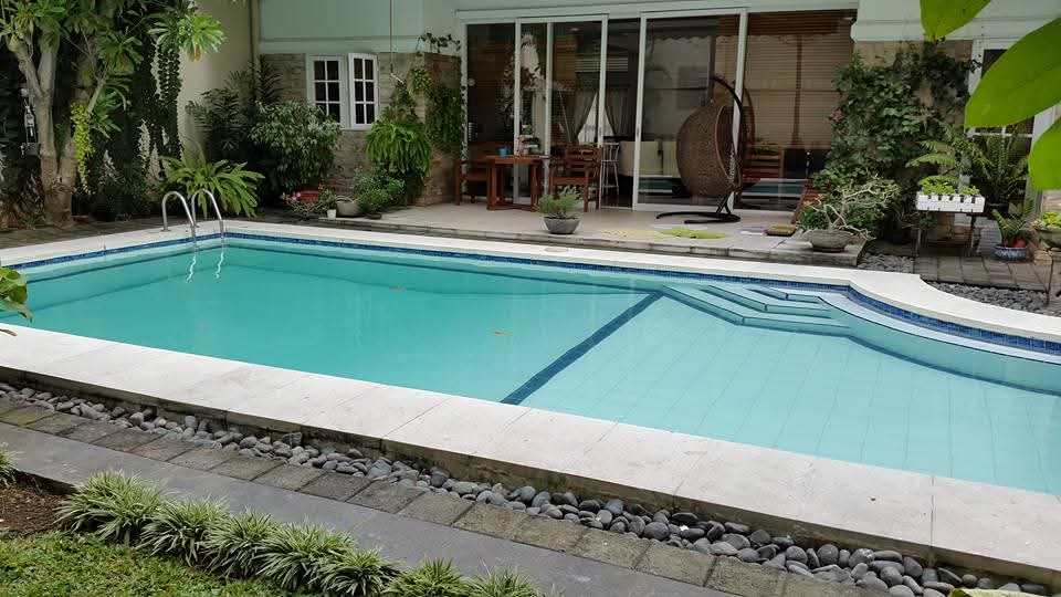 Kolam renang outdoor modern dengan area duduk dan taman hijau asri